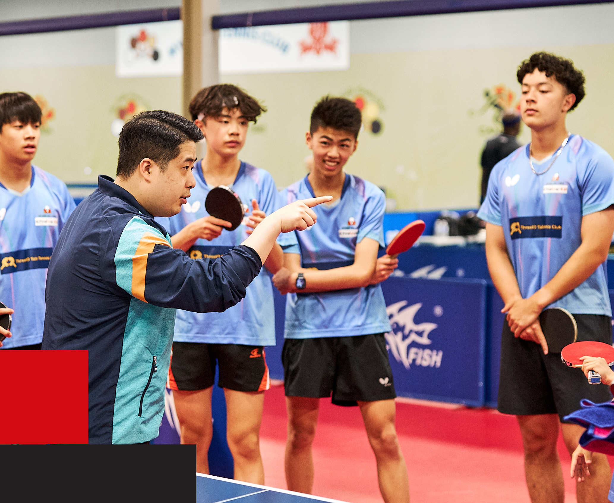 Table Tennis coach instructing team of young players.