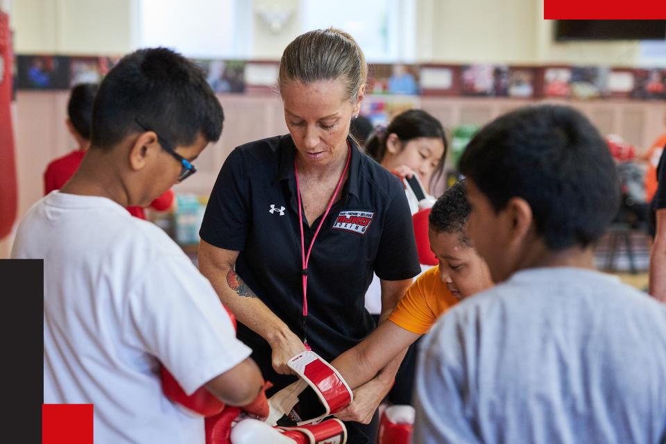 Female boxing coach wrapping wrists of students.