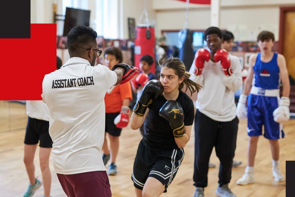 Boxing assistant coach training a lineup of young students.